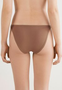 Model van achteren in een bruine onderbroek; zachte huidskleuren en gladde contouren benadrukken de pasvorm en stijl van de stof. Neutrale achtergrond.