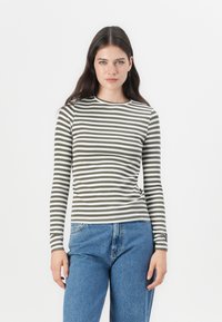Long-sleeve fitted top featuring alternating olive green and white stripes, ribbed texture, and a crew neckline, paired with blue denim jeans.