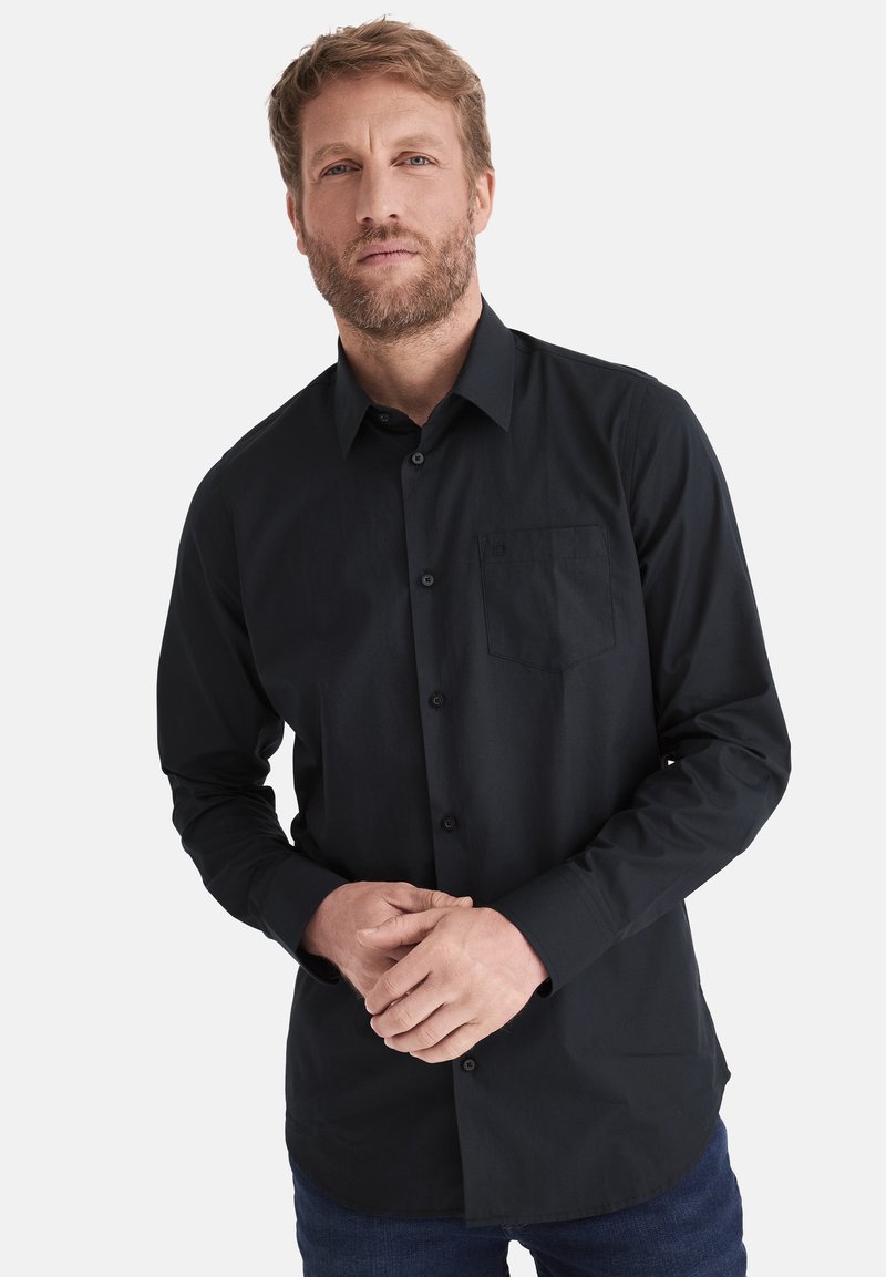 Schwarzes Langarmhemd mit Button-Down-Kragen, Vordertasche und glatter Textur, kombiniert mit dunkelblauen Jeans.