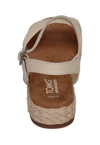 Kremfargede sandaler med flettefletet jute såle, strop av stoff og en sølvfarget spenne. Myk innersåle gir demping. TOMS-merket er synlig.