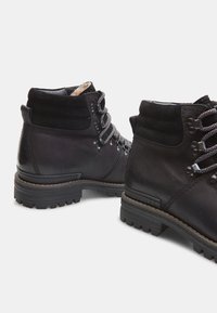 Botas de cuero negro hasta el tobillo con parte superior texturizada, cuello acolchado, seis ojetes de metal y suelas de goma duraderas.