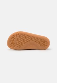 Suola di scarpa in gomma beige con scanalature testurizzate e impronte delle dita. Presenta un logo rotondo e un'indicazione della taglia, progettata per il comfort a piedi nudi.