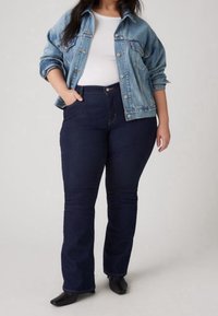 Veste en denim bleu clair à coupe décontractée, t-shirt blanc en dessous, et jean évasé bleu foncé avec des poches et une taille haute.