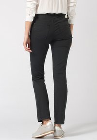 Jean en denim noir avec une coupe slim, dotés de poches arrière et d'une taille mi-haute. Associés à des baskets de couleur claire.