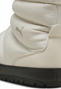 Botín de tobillo blanco hinchado de Puma con parte superior de tela suave, marca gris y suela de goma negra con un patrón de textura.