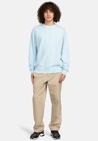 Lys blå sweatshirt med rund hals og ribbede manchetter, parret med beige bukser og sorte sneakers. Glat tekstur, afslappet design.