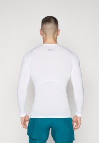 Langærmet hvid atletisk skjorte lavet af fugttransporterende stof, med et tætsiddende design og et lille logo på ryggen.