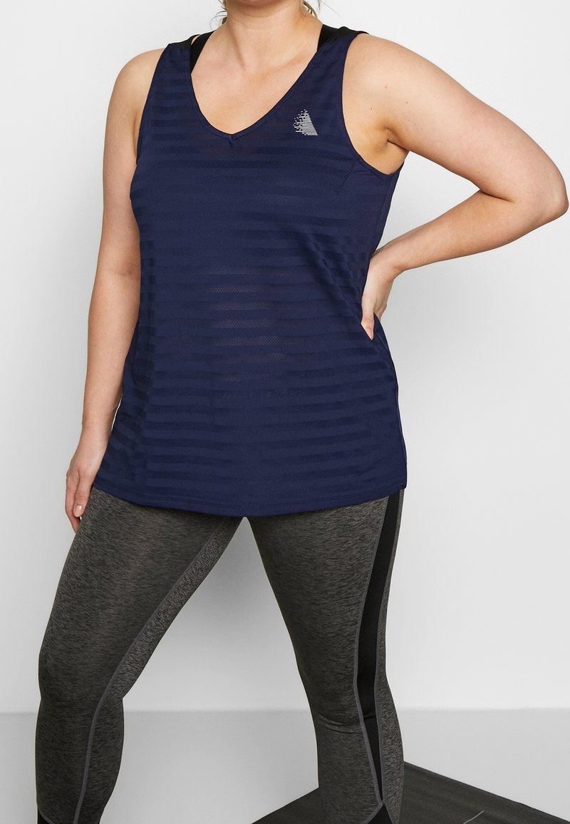 Marineblaues Tanktop mit V-Ausschnitt und horizontalem Streifenmuster. Kombiniert mit grauen Leggings, die schwarze Seitenakzente haben.