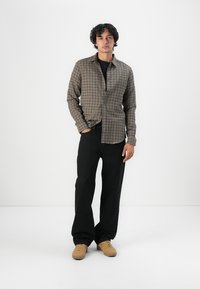 Gray and brown plaid button-up shirt with long sleeves, black pants, and tan shoes. Smooth fabric with a tailored fit.
