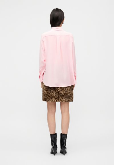 Ροζ σατέν πουκάμισο με μακριά μανίκια και κυρτή ρέλι, σε συνδυασμό με καφέ φούστα με λεοπάρ σχέδιο και μαύρα μυτερά μποτάκια αστραγάλου.