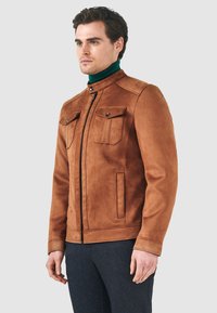 Brun faux suede-jacka med hög krage, dragkedja fram, två bröstfickor och sidfickor. Har stickade detaljer och en figursydd design.