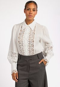 Witte blouse met gestructureerde stof, voorzien van een kanten paneelontwerp, een klassieke kraag en decoratieve kantafwerking op de mouwen. Gecombineerd met grijze pinstripebroek.