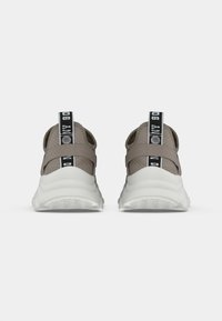 Un paio di scarpe da ginnastica beige e bianche viste da dietro, con linguette nere che presentano testo bianco.