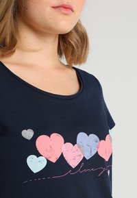 Námořnická modrá bavlněná trička s kulatým výstřihem. Obsahuje srdíčka v různých barvách – růžové, světle modré a šedé – spolu s textem "Miluji tě".