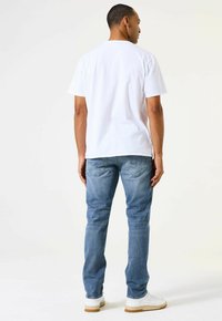 Camiseta de algodón blanca de manga corta, combinada con vaqueros de denim azul claro. Zapatillas blancas con suela de goma. Diseño minimalista, sin patrones.