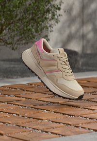 Μπεζ αθλητικά παπούτσια με ροζ λεπτομέρειες και υφή, διαθέτουν σχέδιο με κορδόνια, μαξιλαρωμένο γιακά και χοντρή μαύρη λαστιχένια σόλα.