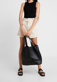 Černá tkaná taška s měkkou texturou a dvojitými uchy, která má prostorný design a mírně povadlý tvar.