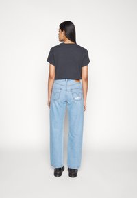 T-shirt preta de algodão cortada com mangas curtas, combinada com jeans de ganga de perna larga em azul claro com bolsos traseiros e uma etiqueta de couro. Sapatos pretos.