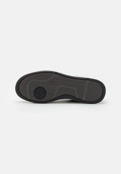 Black rubber shoe sole with a herringbone pattern and circular logo. Flat and textured for grip, featuring raised accents.