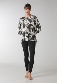 Sort-hvid blomstret top med korte ærmer, løs pasform og slids i siden, parret med sorte leggings. Glat stoftekstur.