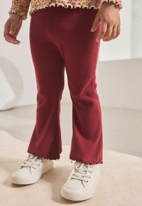 Pantalons rouges à côtes avec des chevilles évasées, dotés d'un ourlet en feston. Assortis à des baskets en toile blanches.