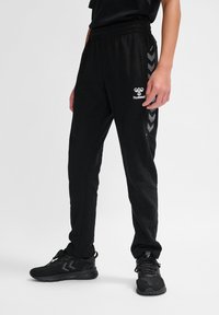 Schwarze Jogginghosen mit elastischem Bund, ausgestattet mit seitlichen Chevron-Streifen und einem weißen Hummel-Logo auf dem linken Oberschenkel.