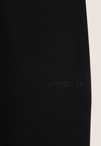 Pantalones de tejido elástico negro con un discreto logo de Freddy grabado en el costado, que presentan líneas limpias y una textura suave.