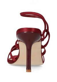 Red high-heeled sandal featuring a satin upper, open back, and crisscross straps. Slim stiletto heel with a beige sole.