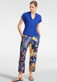 Top azzurro a maniche corte abbinato a pantaloni navy a motivo floreale con colori vivaci, più sandali con cinturini. Tessuto dalla texture liscia.