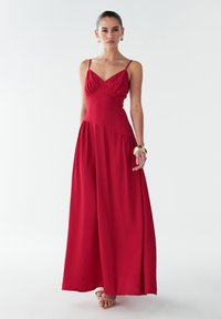 Vestido maxi sin mangas de color rojo con un corsé ajustado, detalles plisados y una falda fluida. Tela suave con una textura delicada.