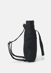 Schwarzer Stoffrucksack mit runder Basis, verstellbarem Kordelverschluss und zwei langen, flachen Schultergurten. Minimalistisches Design und Textur.