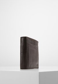 Portafoglio in pelle marrone con superficie texturizzata, design bi-fold e un singolo slot per carte esterno su un lato, esposto in posizione verticale su una superficie bianca.
