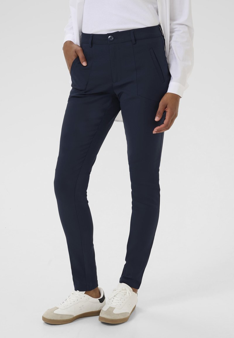 Pantalons ajustés bleu marine avec poches avant, en tissu lisse. Associés à des baskets blanches avec un accent beige et noir.