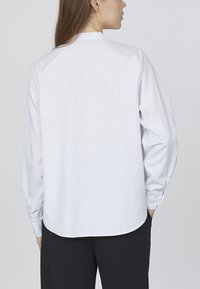 Hvid skjorte med knapper og lodrette blå striber, lange ærmer, afrundet kant og båndkrave. Glat overflade og skræddersyet pasform.