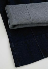 Granatowe dżinsy z podwiniętym szarym mankietem, gładka tekstura, kontrastowe przeszycia i staranne wykończenie dołu.