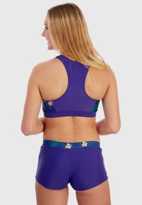 Ensemble de maillot de bain violet comprenant un haut avec dos nageur orné de motifs floraux et un short assorti. Tissu doux avec une texture légèrement brillante.
