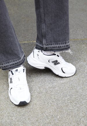 Białe buty do biegania z czarnymi akcentami i teksturowaną siateczką. Sparowane ze spranym ciemnoszarym dżinsem, z widocznym szczegółowym przeszyciem i fakturą.