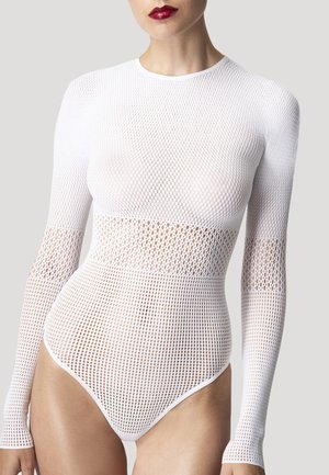 Frau trägt einen weißen, langärmeligen Netz-Body mit unterschiedlichen Mustern und roten Lippenstift vor einem schlichten hellen Hintergrund.