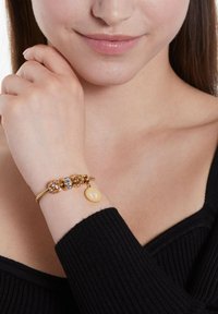 Gouden armband met drie decoratieve kralen, waaronder roze stenen en een zilveren accent, met een gele bedel waarop voetafdrukken te zien zijn.