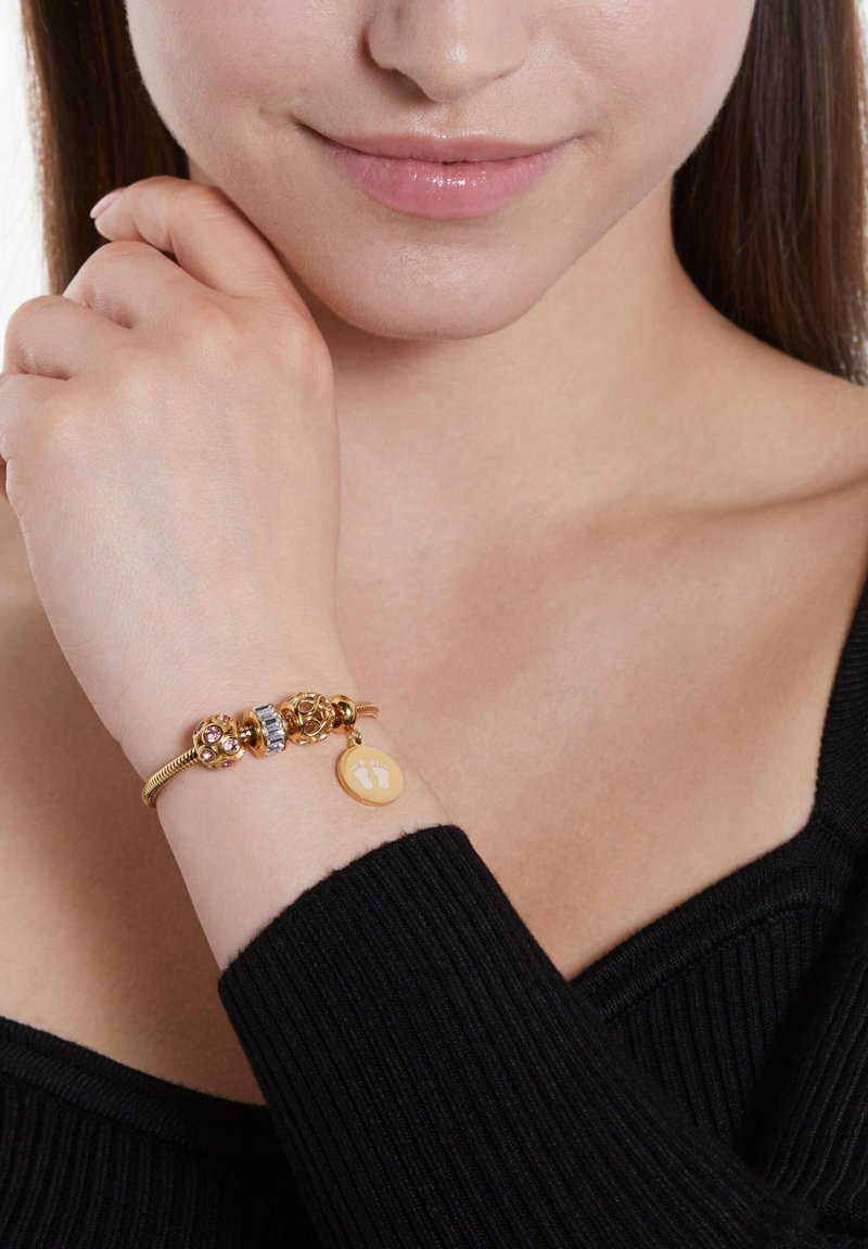 Gouden armband met drie decoratieve kralen, waaronder roze stenen en een zilveren accent, met een gele bedel waarop voetafdrukken te zien zijn.