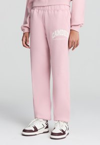 Pantaloni della tuta rosa chiaro con elastico in vita, con la parola "CAMDEN" stampata in bianco sulla gamba sinistra. Tessuto morbido e texturizzato.