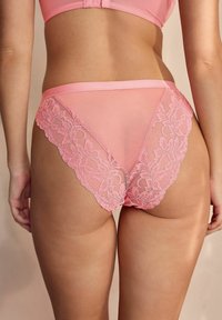 Pantalone s rozim čipkastim rubom koji imaju prozirne mrežaste panele i cvjetni čipkasti uzorak duž rubova, naglašavajući delikatnu teksturu.