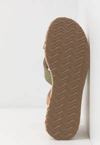 Sandale verte et orange avec une semelle en caoutchouc texturée à motif en vagues, présentant un accent en tissu fleuri autour du bord.