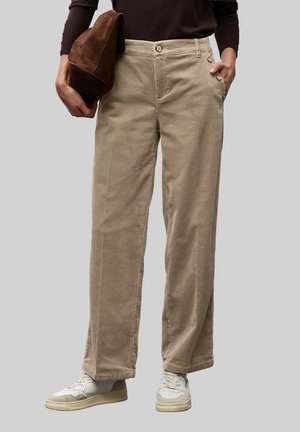 Beige Cordhosen mit geradem Schnitt, ausgestattet mit zwei Knöpfen an der Seite, kombiniert mit einer braunen Stoff-Clutch und weißen Sneakers.