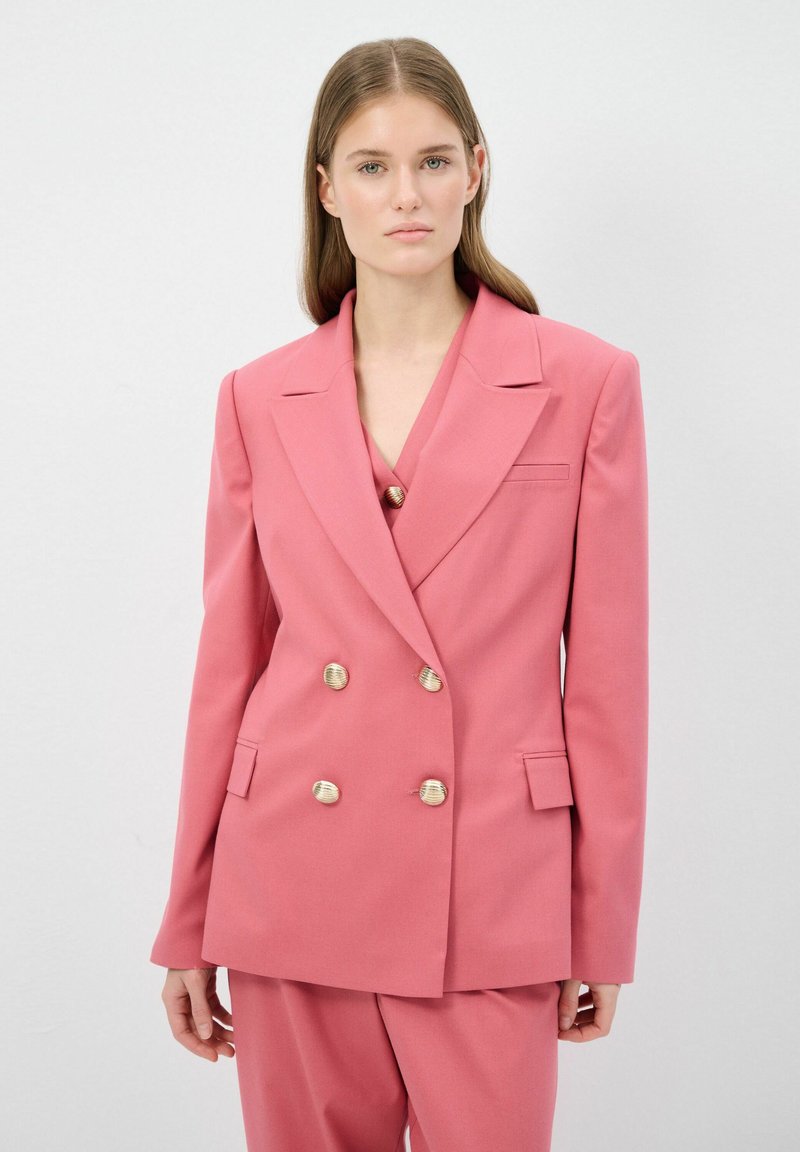 Kaksoisnappinen bleiseri kirkkaan vaaleanpunaisesta kankaasta, jossa on kultasävytteiset napit, terävät läpät ja etutaskut rakenteellisella istuvuudella.