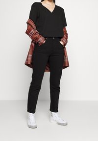 Sort V-hals t-shirt lagd med en rødternet skjorte, parret med sorte jeans og hvide high-top sneakers med sorte accenter.