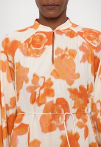 Blumenkleid mit großen orangefarbenen Blumen auf cremefarbenem Hintergrund, einem Schlüssellochausschnitt und einem Kordelzugbund aus leichtem Stoff.