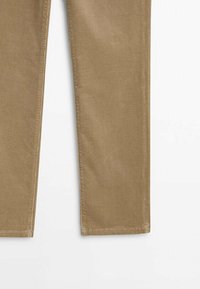 La moitié inférieure d’un pantalon droit en velours côtelé kaki, avec une texture visible et des ourlets cousus, sur fond blanc.