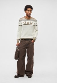 Pletený sveter v krémovej farbe s motívmi sobov a textúrovaným dizajnom, doplnený voľnými hnedými nohavicami a tmavohnedou taškou.