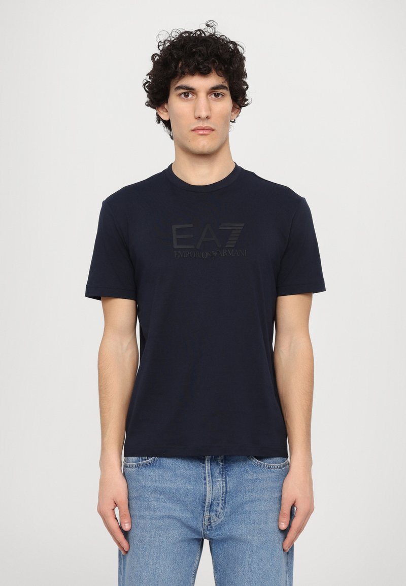 Μπλε κοντομάνικο μπλουζάκι από βαμβάκι, με ανάγλυφο μαύρο λογότυπο στο μπροστινό μέρος. Στρογγυλή λαιμόκοψη και άνετη εφαρμογή.